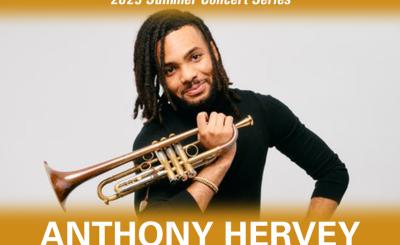 Anthony Hervey wearing black long sleeve sitting down with trumpet in hand in front of a gray background