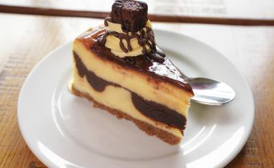 Slice of vanilla cake with chocolate in between and on top on a plate on a table lit by a nearby window