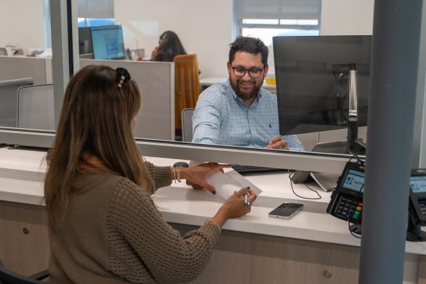 Employee smiles behind glass and hands paper to client