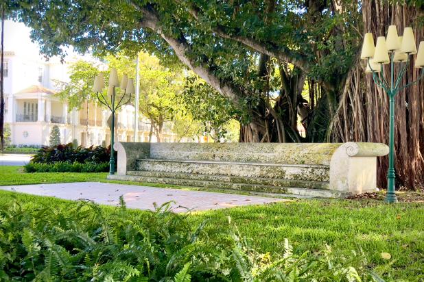 Two lamps stand on the sides of a coral sculpture in shape of a couch. Behind a large tree.