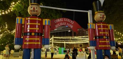 Two giant toy soldiers stand by the entrance of a lit park at night