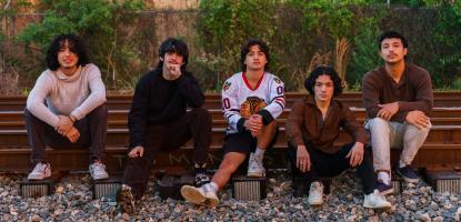 5 band members sit on a rail track and gravel during the day