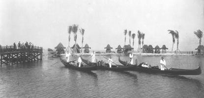 Black and white photo of men in white clothing rowing gondolas on a river