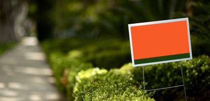 An orange and black sign next to a short hedge on a lawn