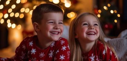 Two children in matching red with white star pajamas laugh. They each have a stack of pancakes in front of them. 