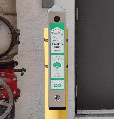 Silver cigarette receptacle strapped to a yellow post. On it, a green sticker with information