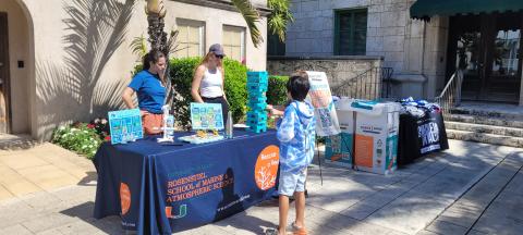 On a sunny day, a child speaks with two women behind a sustainability booth