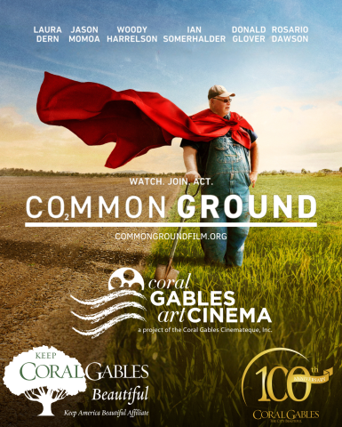 A man with a cap looks over a farm with a red cape billowing in the wind