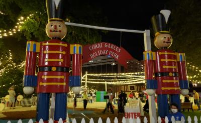 Two giant toy soldiers stand by the entrance of a lit park at night