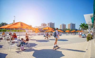 Beautiful sunny day and blue sky, college students sit under orange umbrellas while a man skateboards past the plaza