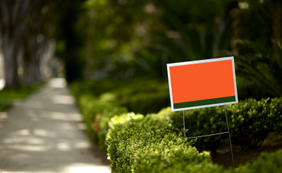 An orange and black sign next to a short hedge on a lawn