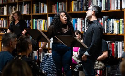 Actors perform with a background of book shelves and books