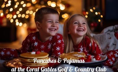 Two children in matching red with white star pajamas laugh. They each have a stack of pancakes in front of them. 