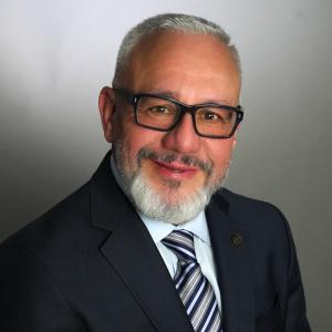 Jose Gomez in a dark suit in a gray background